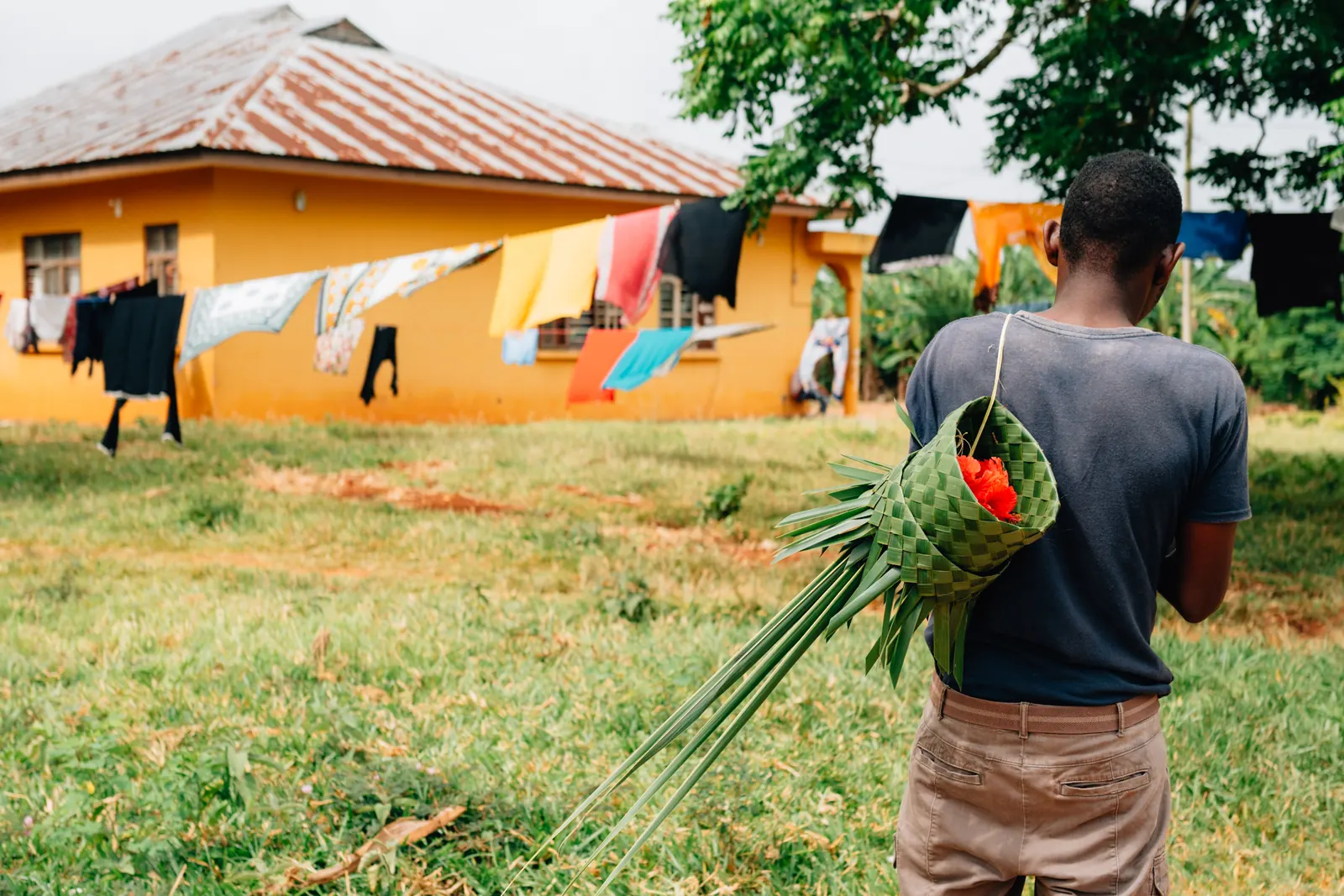 Voyageur vu de dos portant un panier tressé en feuille de palmier garni de fleurs d'hibiscus