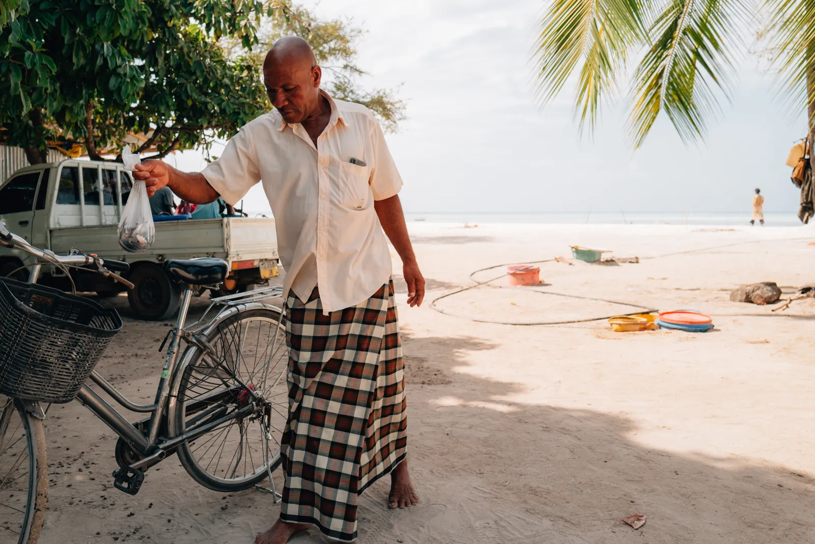 Homme swahili avec son vélo sur la plage, scène de vie locale.